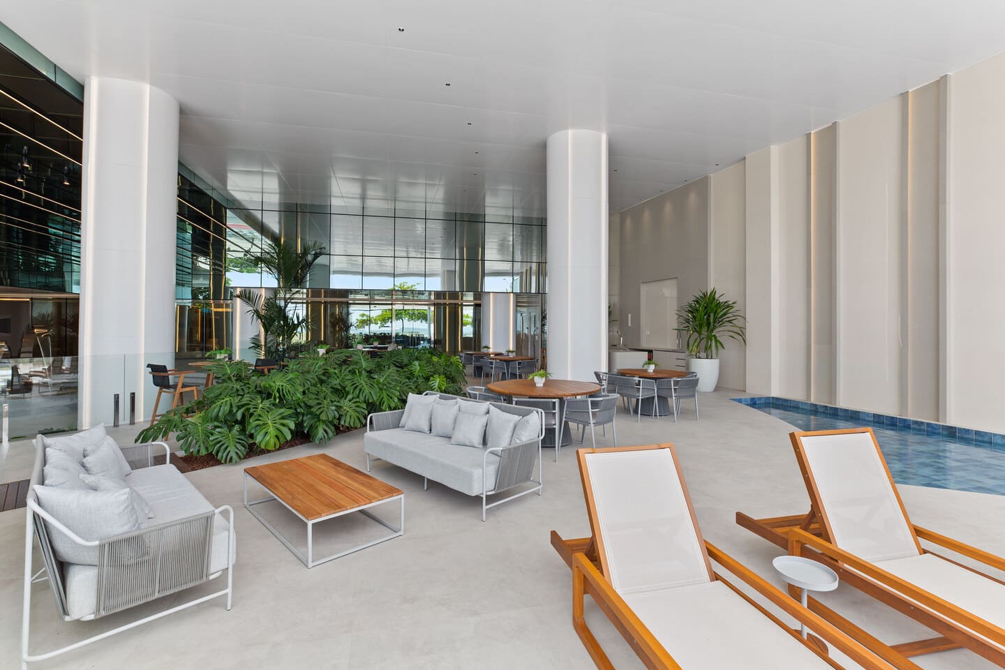 Lounge coberto anexo às piscinas com sofás aconchegantes, iluminação cênica e vegetação tropical