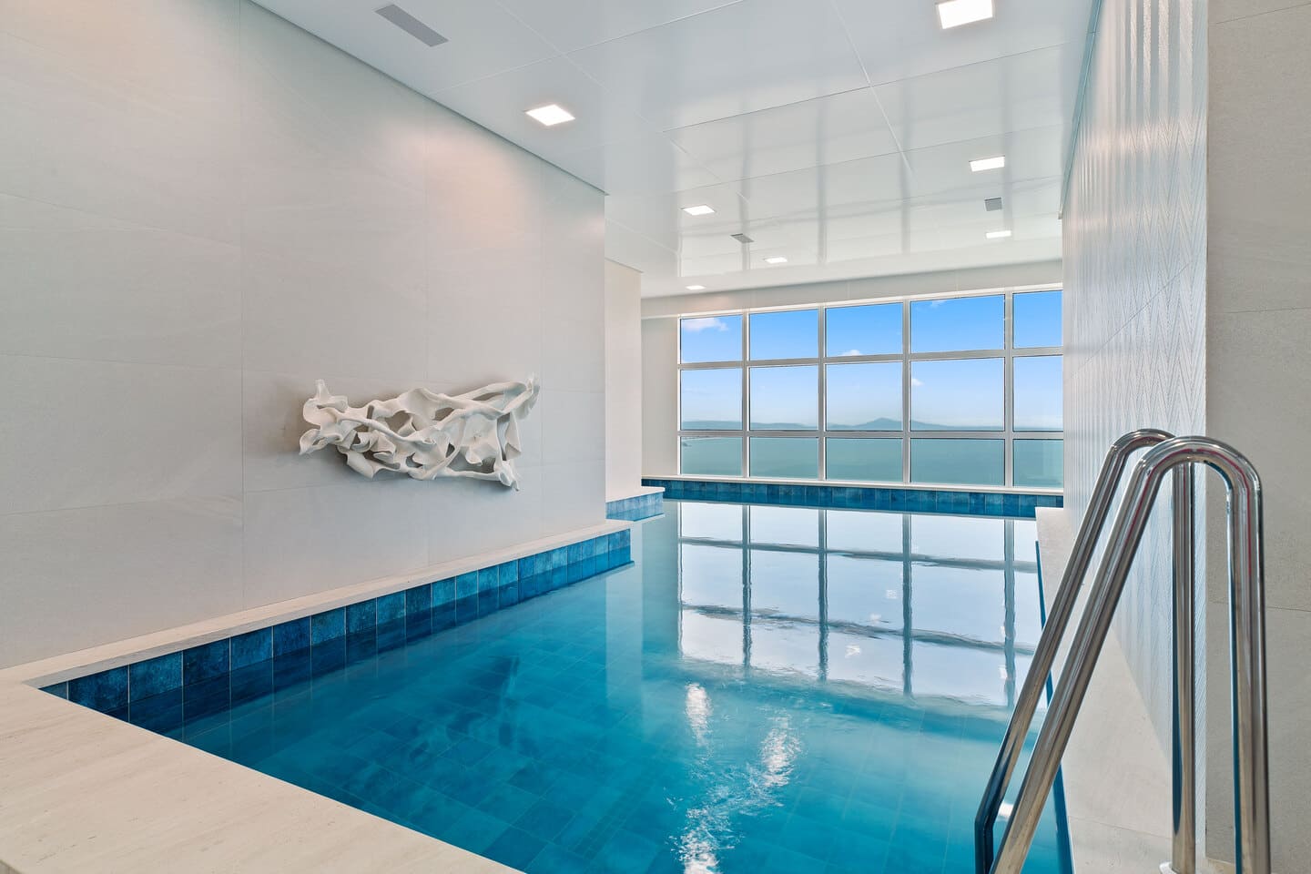 Piscina coberta e aquecida do One Tower com raia para natação e grandes panos de vidro voltados para a orla marítima