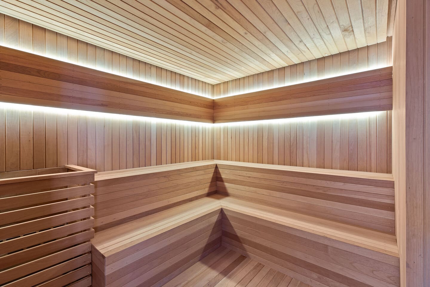 Sauna seca em madeira nobre clara de cedro com bancos ergonômicos e iluminação linear indireta em LED