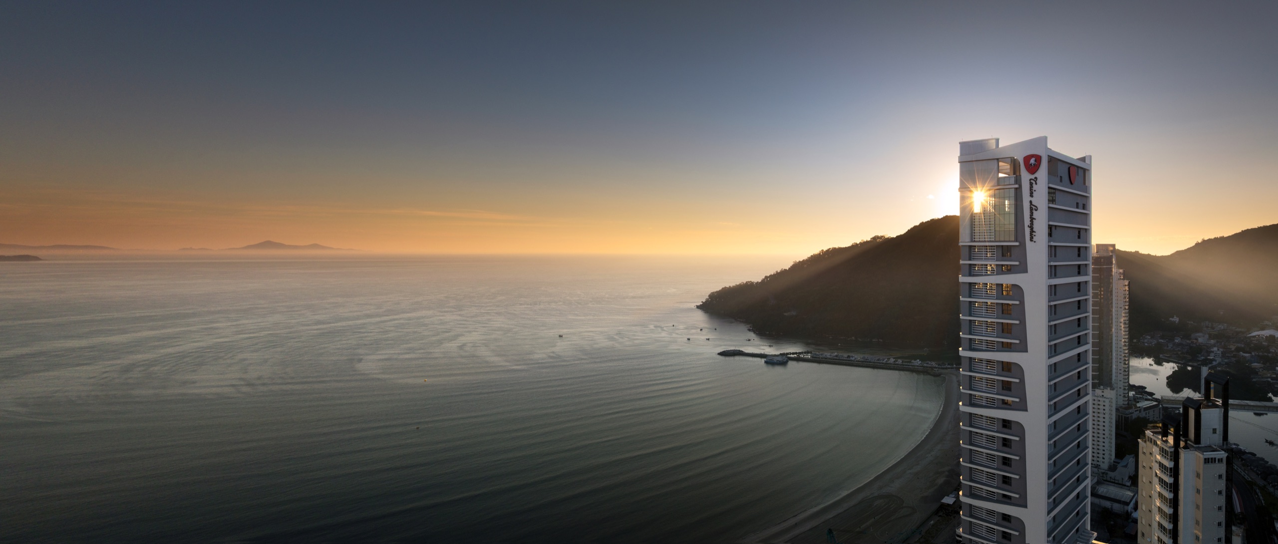 Fotografía panorámica del amanecer atravesando el coronamiento de Tonino Lamborghini Residences sobre la bahía de Balneário Camboriú y la desembocadura del río Camboriú