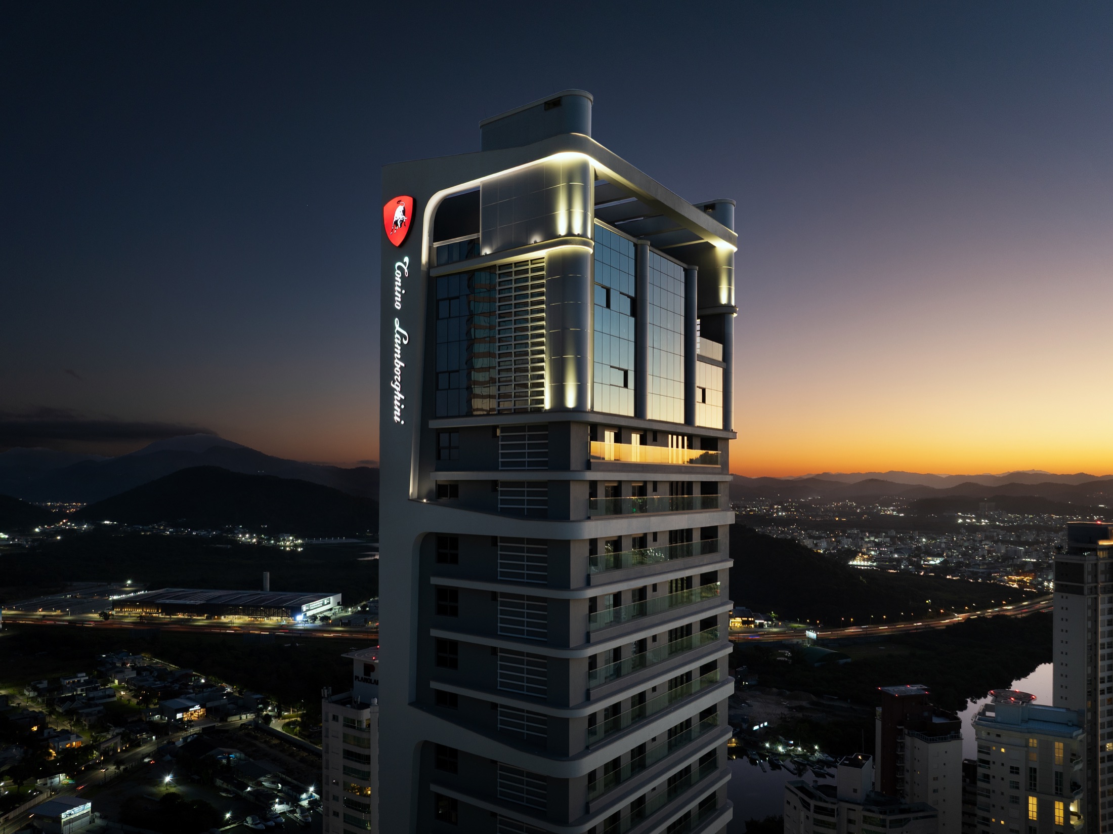 Fotografía real del coronamiento iluminado de Tonino Lamborghini Residences al atardecer, destacando el letrero vertical y el escudo rojo del toro Miura