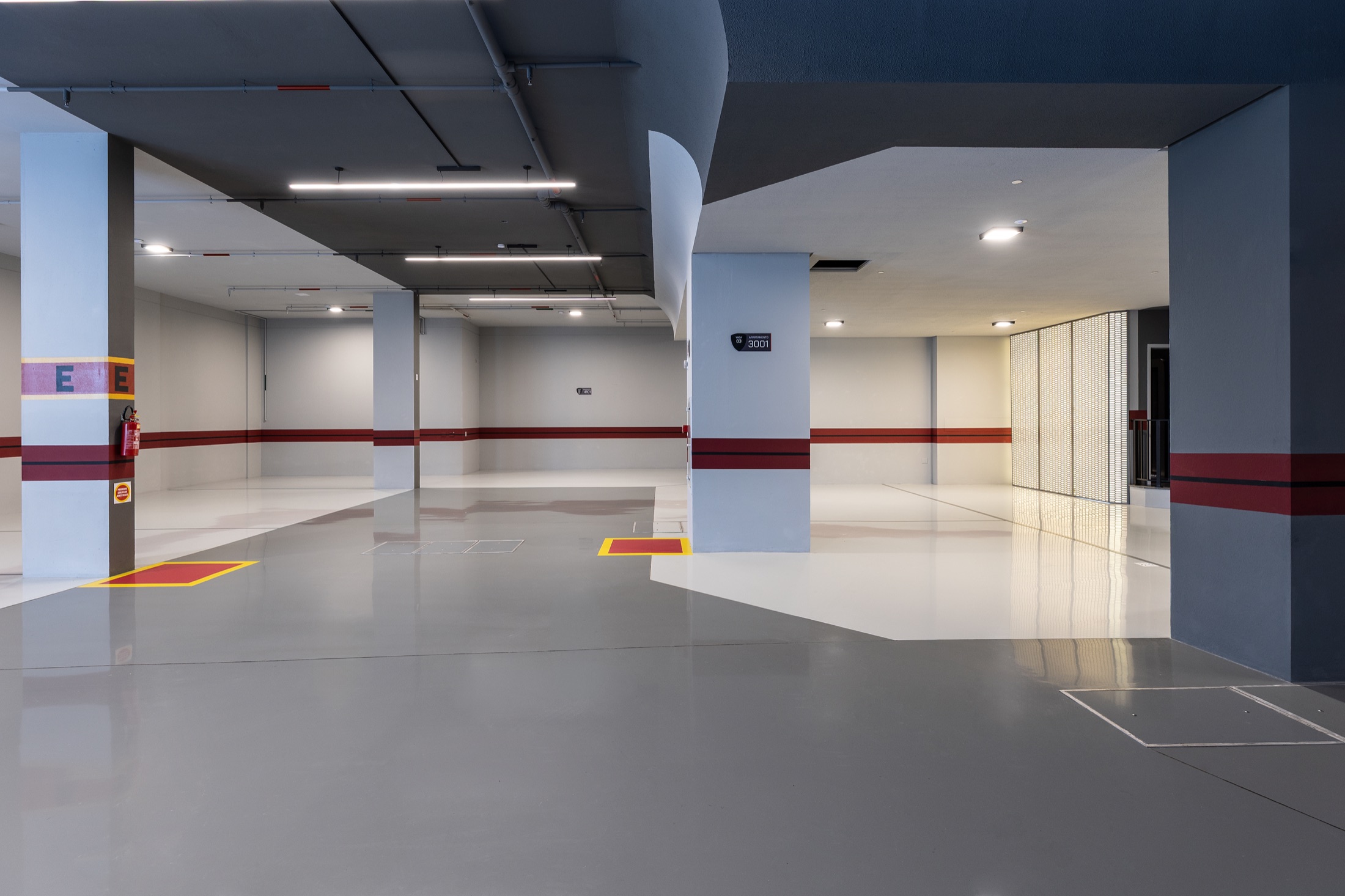 Fotografía real del garaje entregado de Tonino Lamborghini Residences con piso en pintura epoxi brillante, franjas en rojo y grafito, placas con el escudo de la marca e iluminación lineal