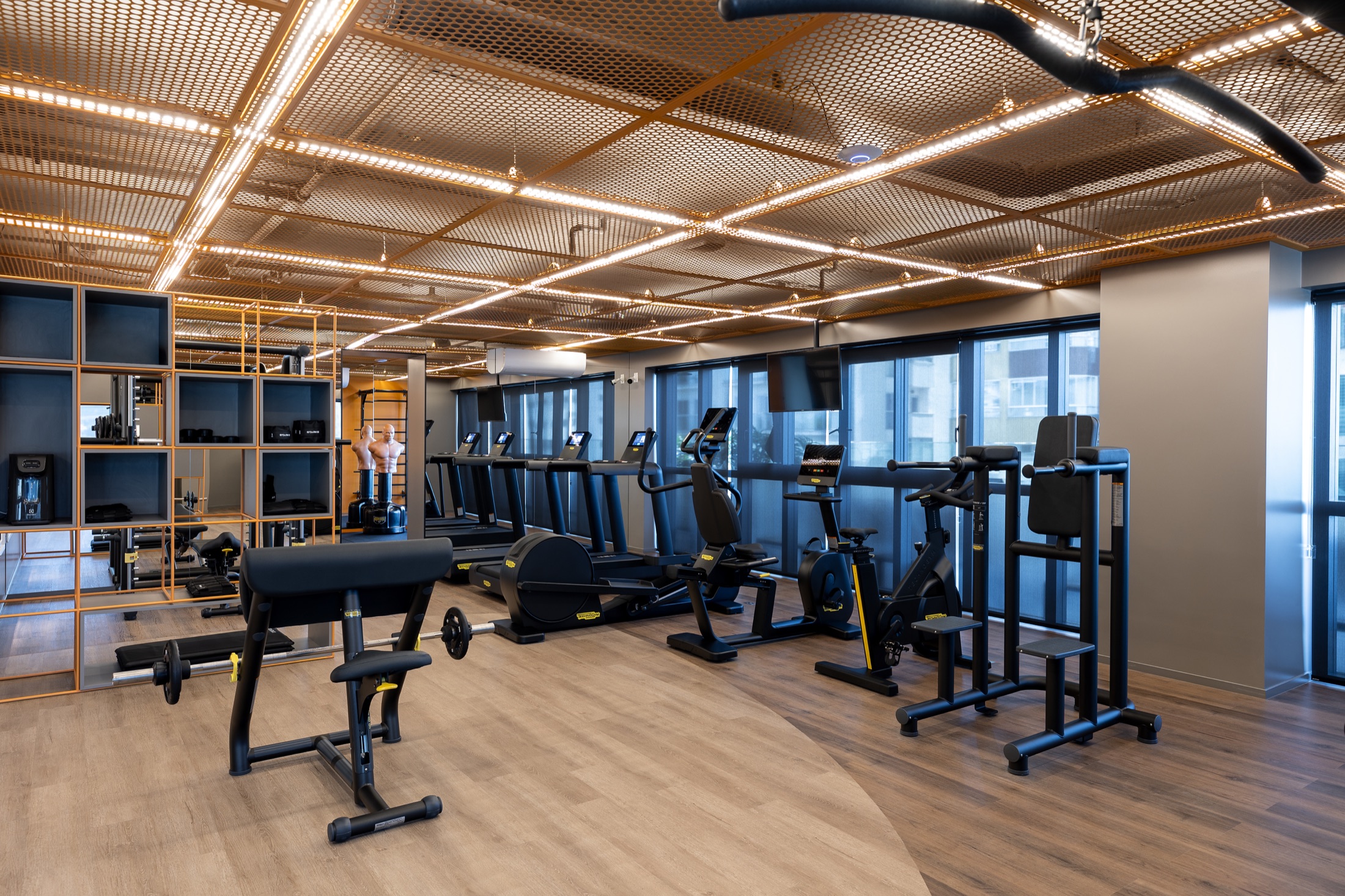 Fotografía real del Gimnasio entregado con equipos Technogym y techo en malla metálica dorada iluminada por líneas de LED