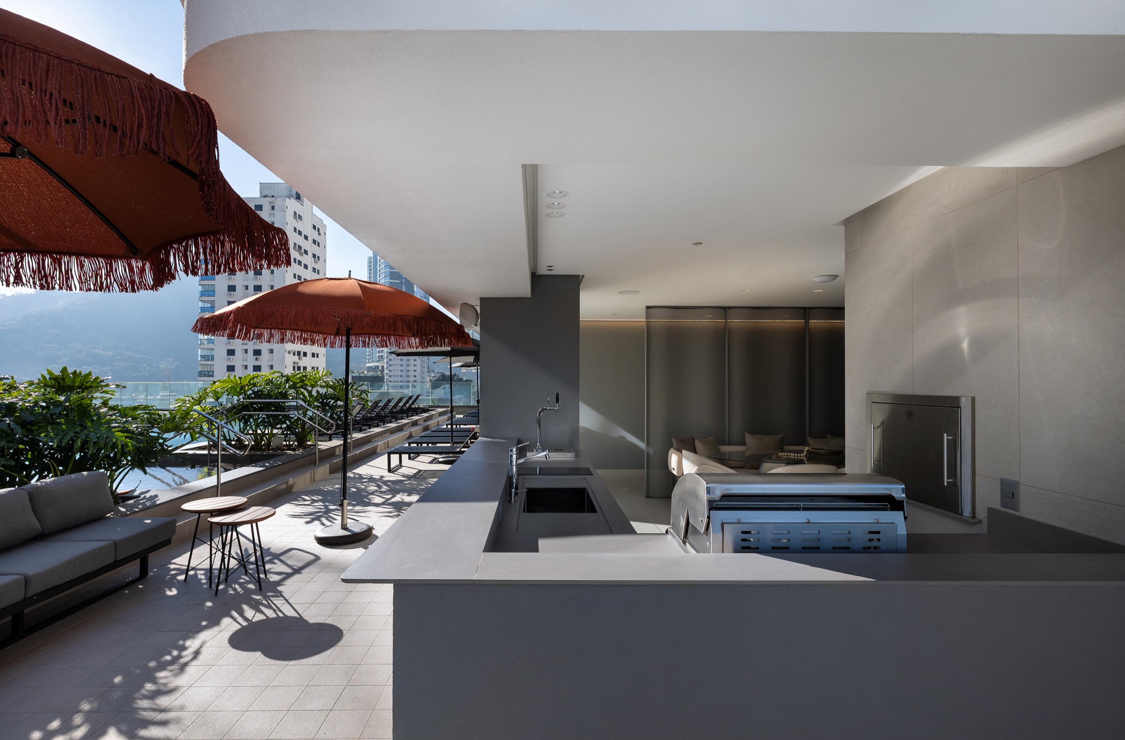 Fotografía real del Espacio Grill exterior junto al deck de la piscina con char-broiler, parrilla y sombrillas terracota