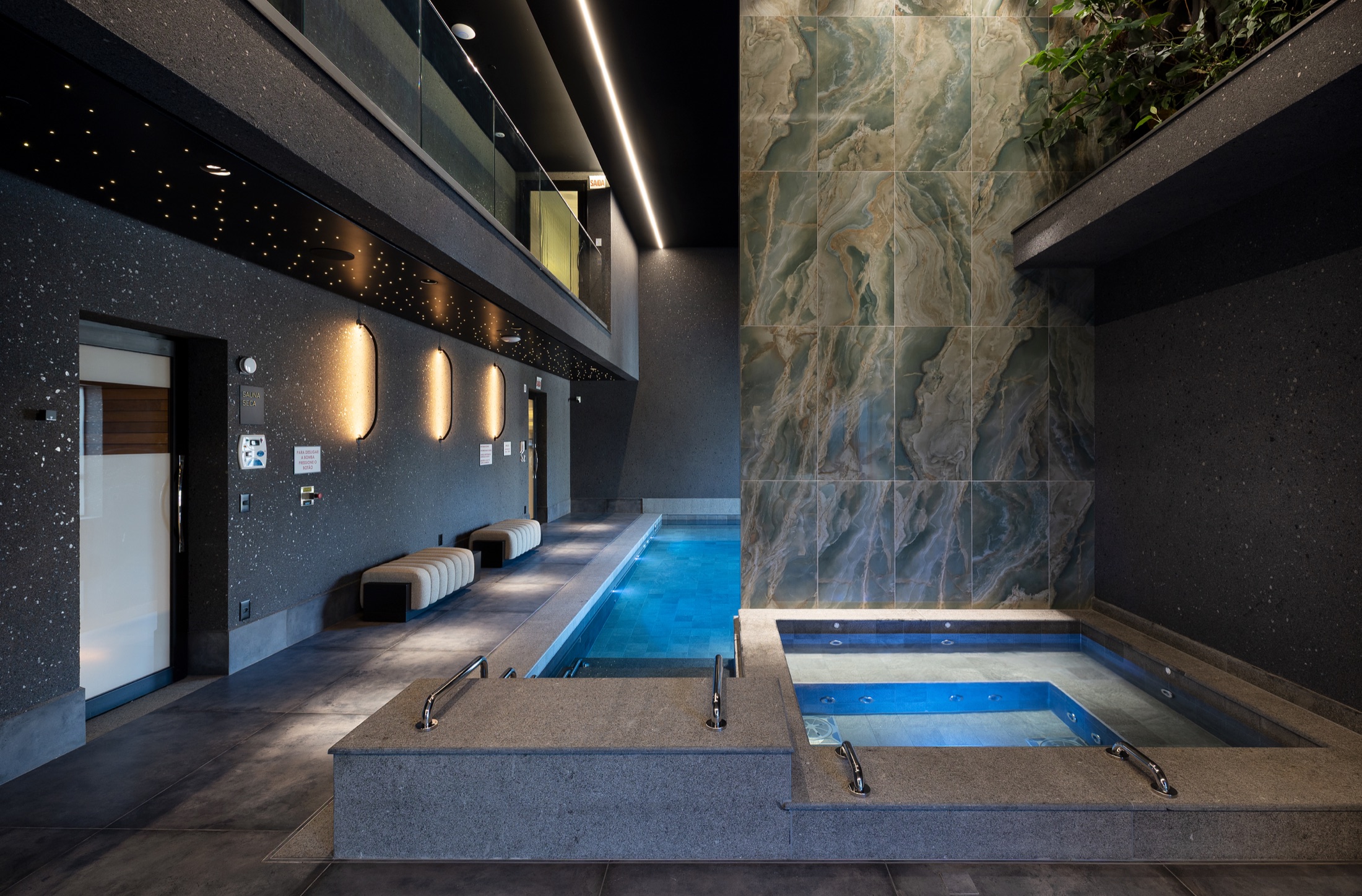 Fotografía real de la piscina interior climatizada con revestimiento en ónix verde, hidromasaje y techo negro con fibras ópticas