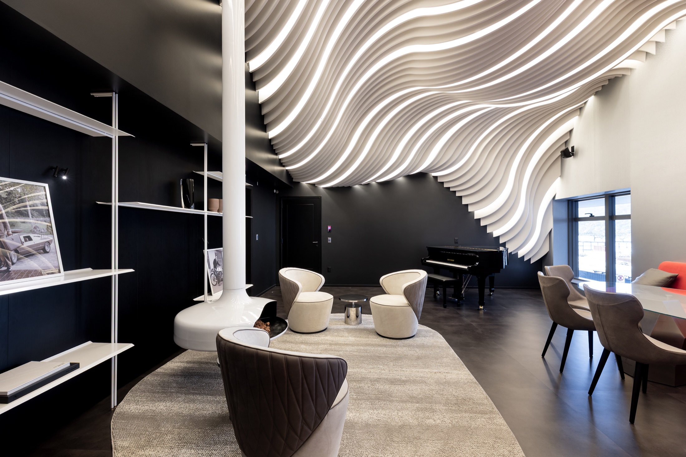 Fotografía real del Tonino Lamborghini Lounge en el entresuelo, mostrando el techo paramétrico en ondas blancas, el piano de cola negro, la chimenea suspendida y el mobiliario italiano en cuero